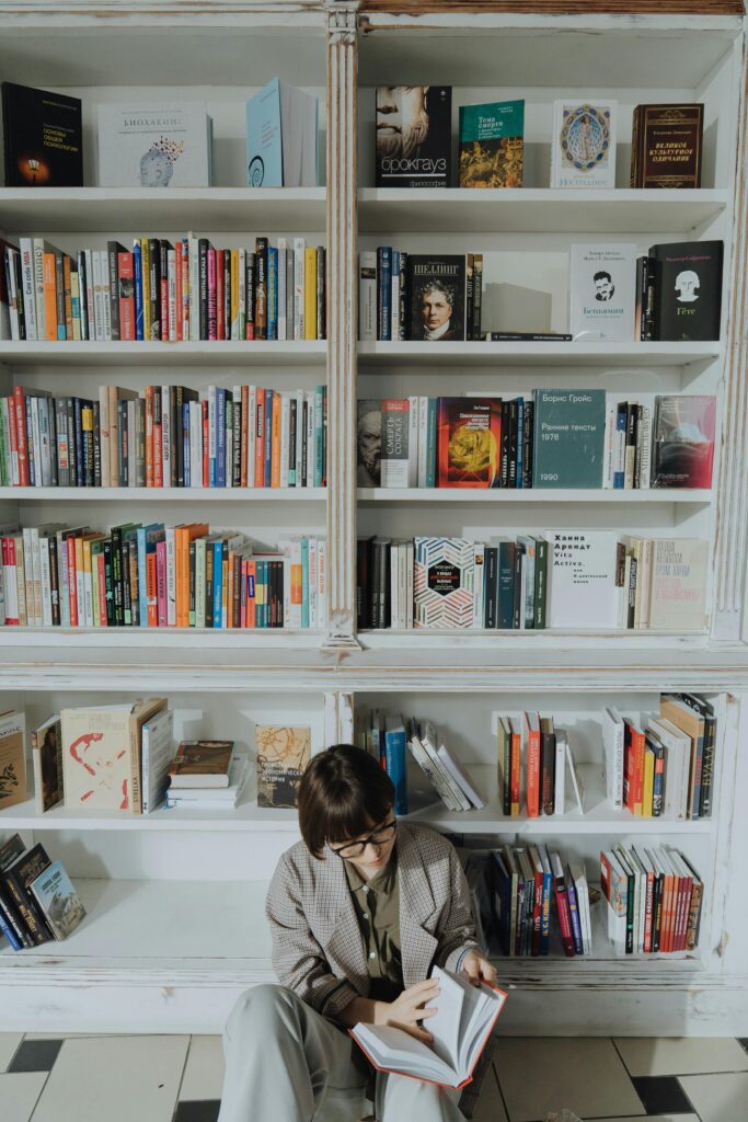 Woman reading a book in a modern library setting, surrounded by diverse literature.
